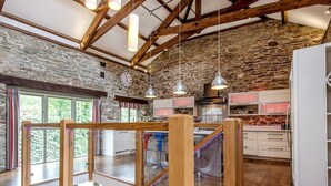A spacious kitchen with stone walls, wooden beams, and modern appliances. - Mill Barn (Kingsbridge)