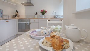 A modern kitchen with white cabinets, a stainless steel range hood, and a countertop with a polka dot tablecloth. There are plates of scones and a white teapot on the table. - Torrings Barn (Kingsbridge)