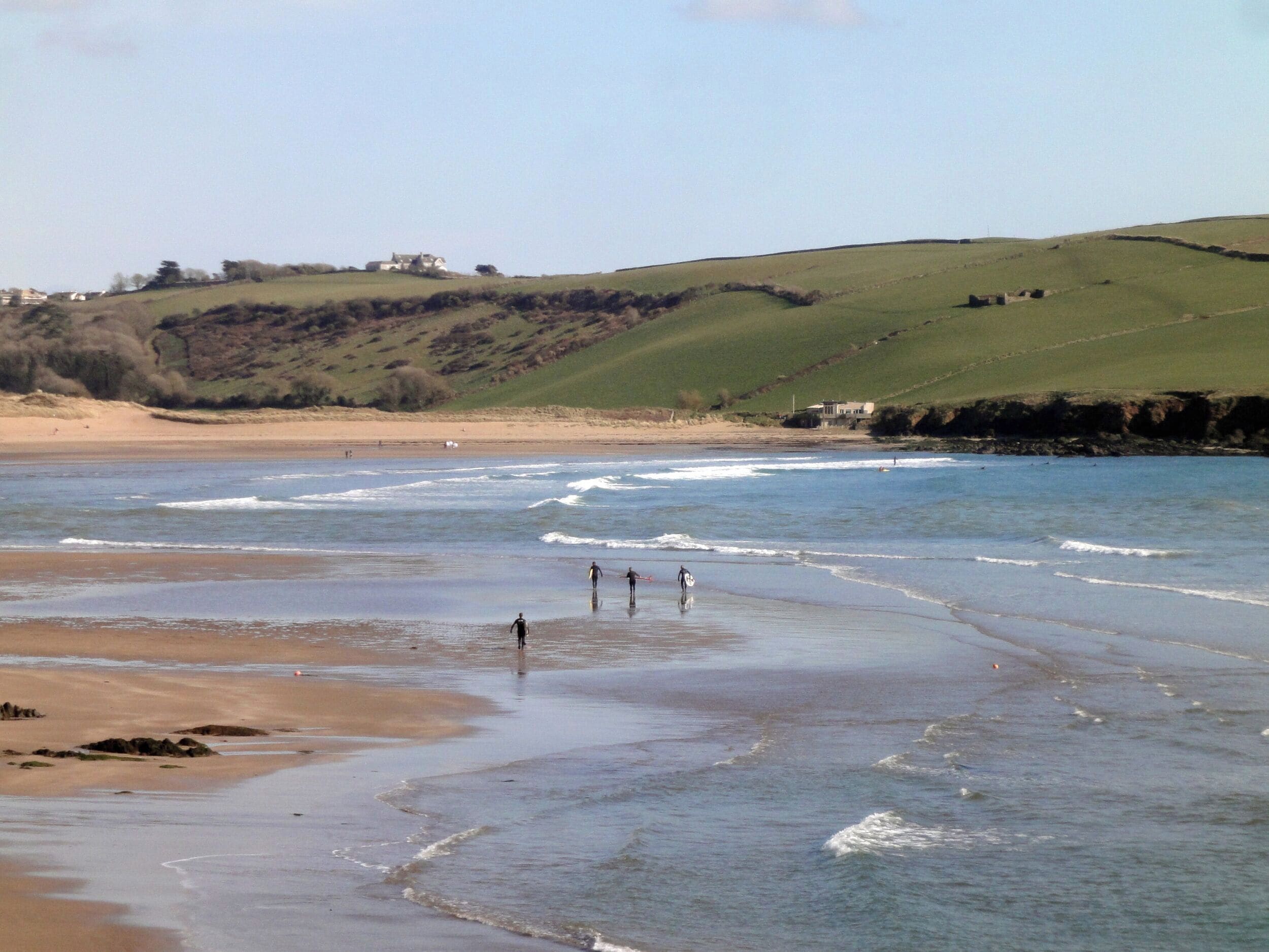 A beach with waves, a sandy shore, and a grassy hill in the background.