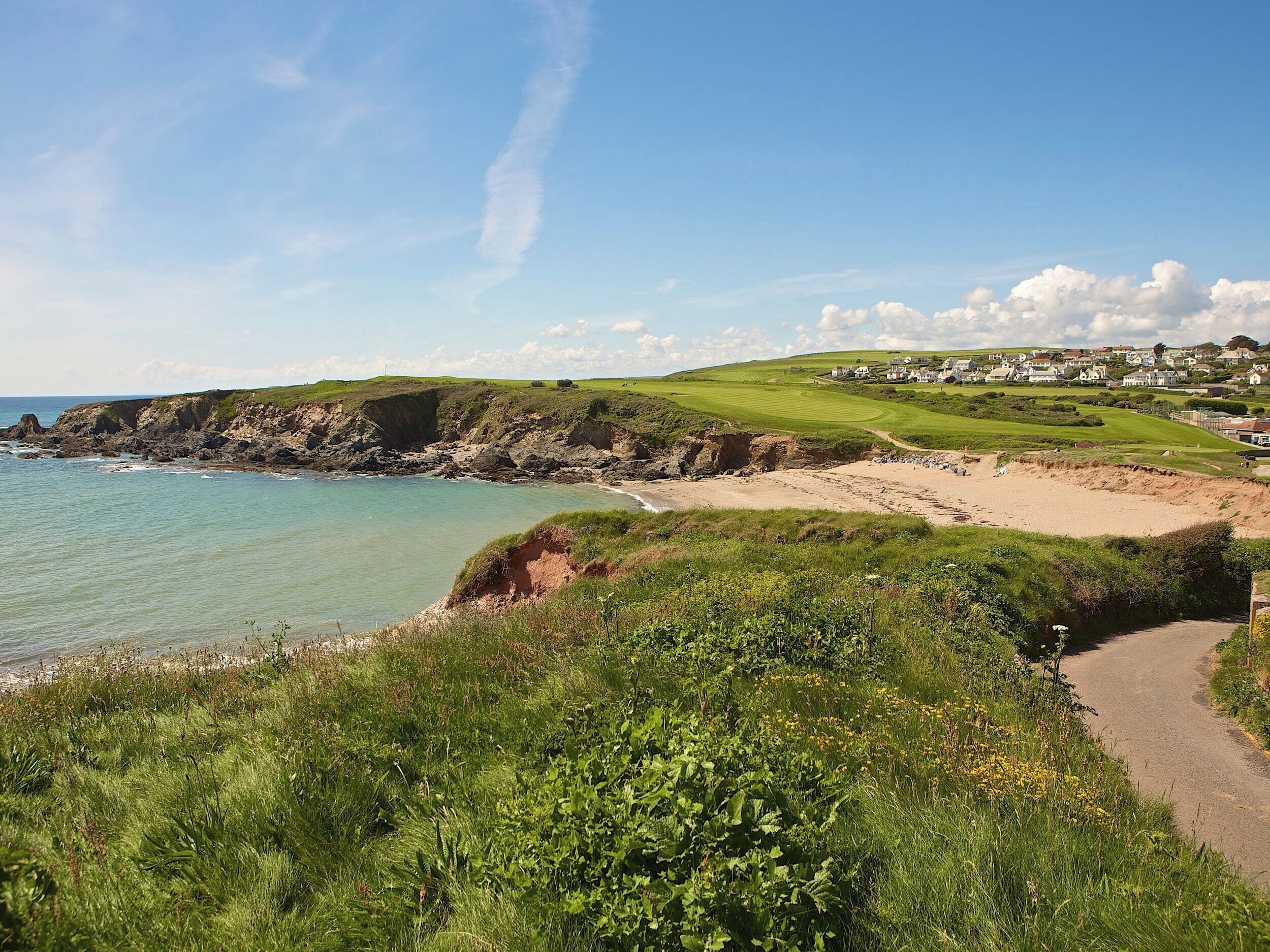 Un paysage côtier avec une plage de sable, des collines verdoyantes et un terrain de golf.
