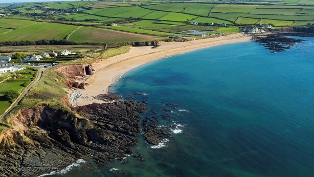 A coastal landscape with a sandy beach, rocky shoreline, and green fields in the background. - Torrings Barn (Kingsbridge)
