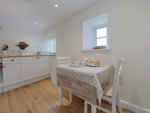 Une cuisine moderne avec des meubles blancs, un plan de travail en bois et une table à manger recouverte d’une nappe à pois. Il y a une fenêtre au-dessus de l’évier et une petite étagère où sont disposés des objets décoratifs.