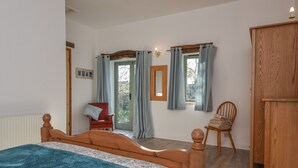 A bedroom with a wooden bed, a chair, a wardrobe, and a window with curtains. - Bradbridge Barn (Plymouth)