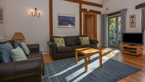 A living room with a brown sofa, a wooden coffee table, and a TV on a wooden stand. - Bradbridge Barn (Plymouth)