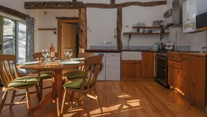 A wooden dining table with chairs, a kitchen with wooden cabinets, a dishwasher, and a microwave. - Bradbridge Barn (Plymouth)