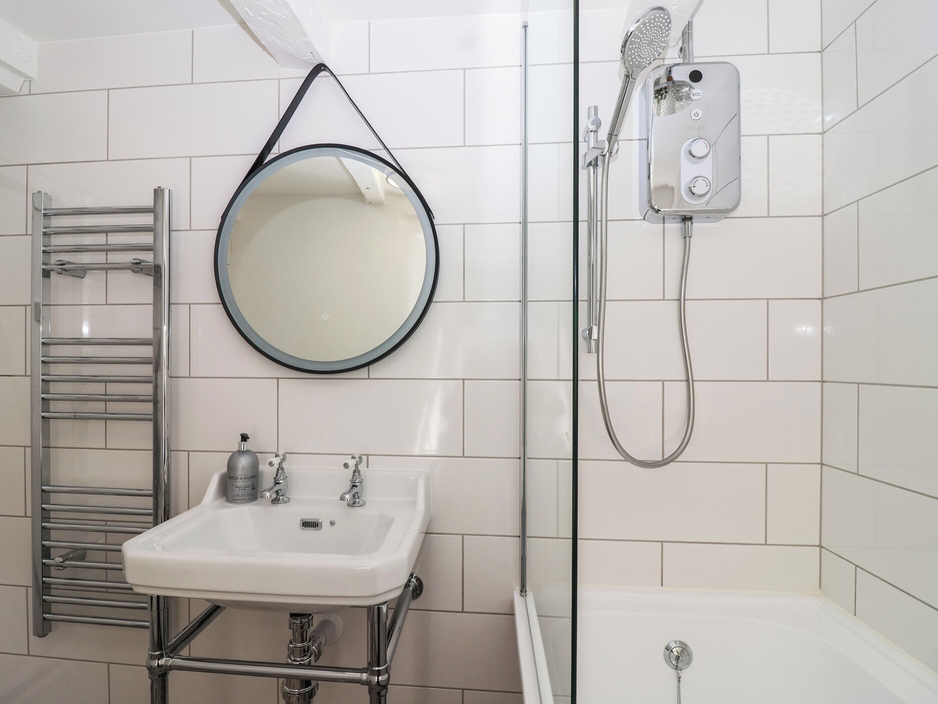 Ein modernes Badezimmer mit rundem Spiegel, Waschbecken, Handtuchhalter und Dusche mit Duschbrause.