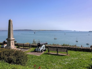 A monument with a cannon, a bench, and a grassy area with flowers. - Cousham Cottage (Torpoint)