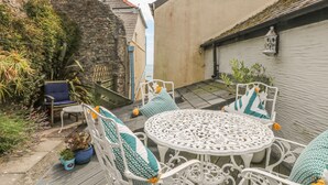 Une terrasse dotée de meubles en osier blanc, de plantes en pot et d’un mur en pierre.