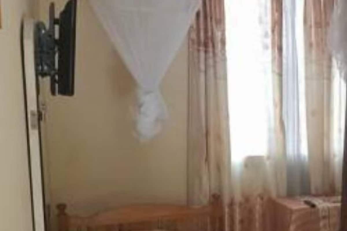 Un dormitorio con cama, mesita de noche, silla y ventana con cortinas.