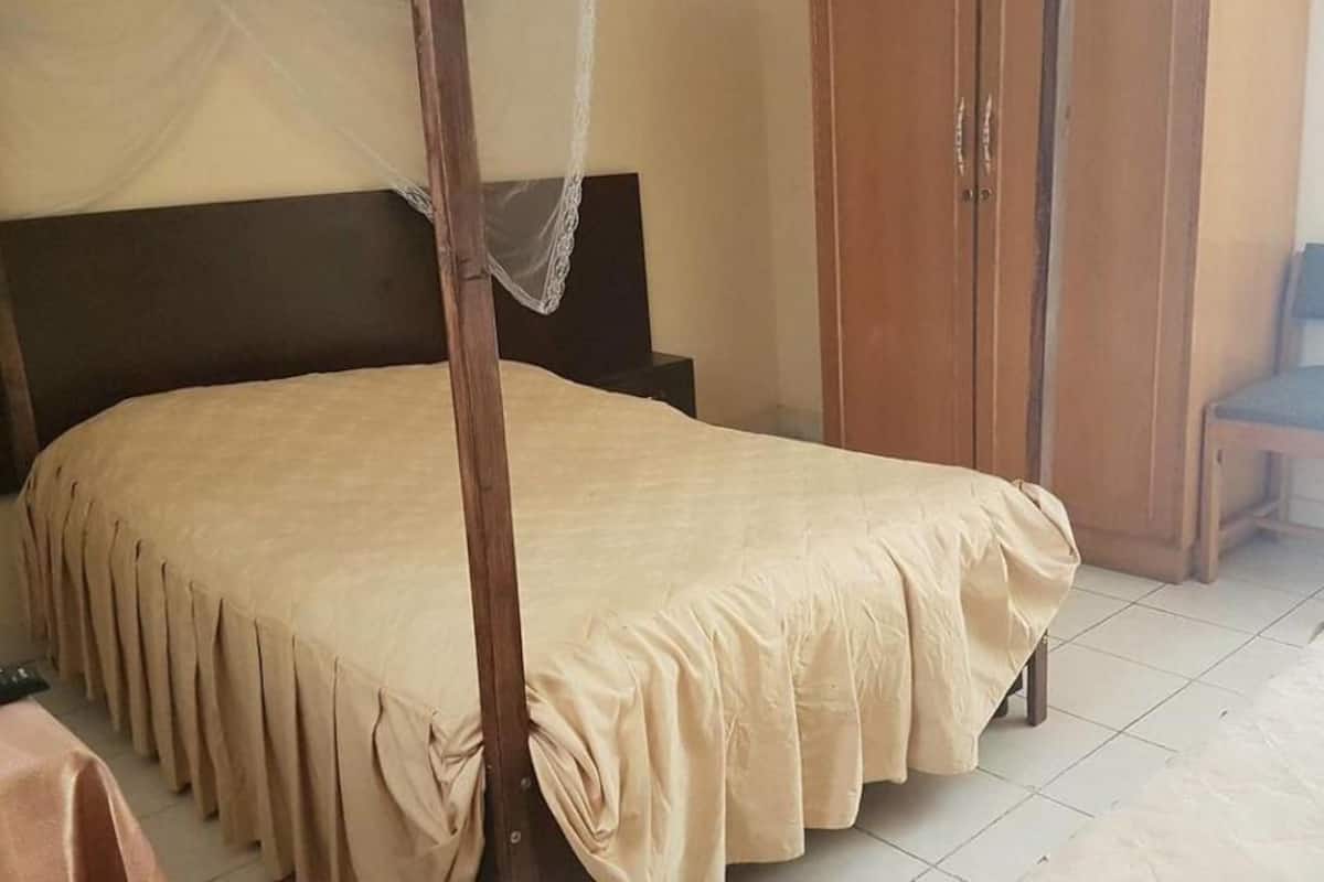 Un dormitorio con cama, armario de madera, una silla y mosquitera.
