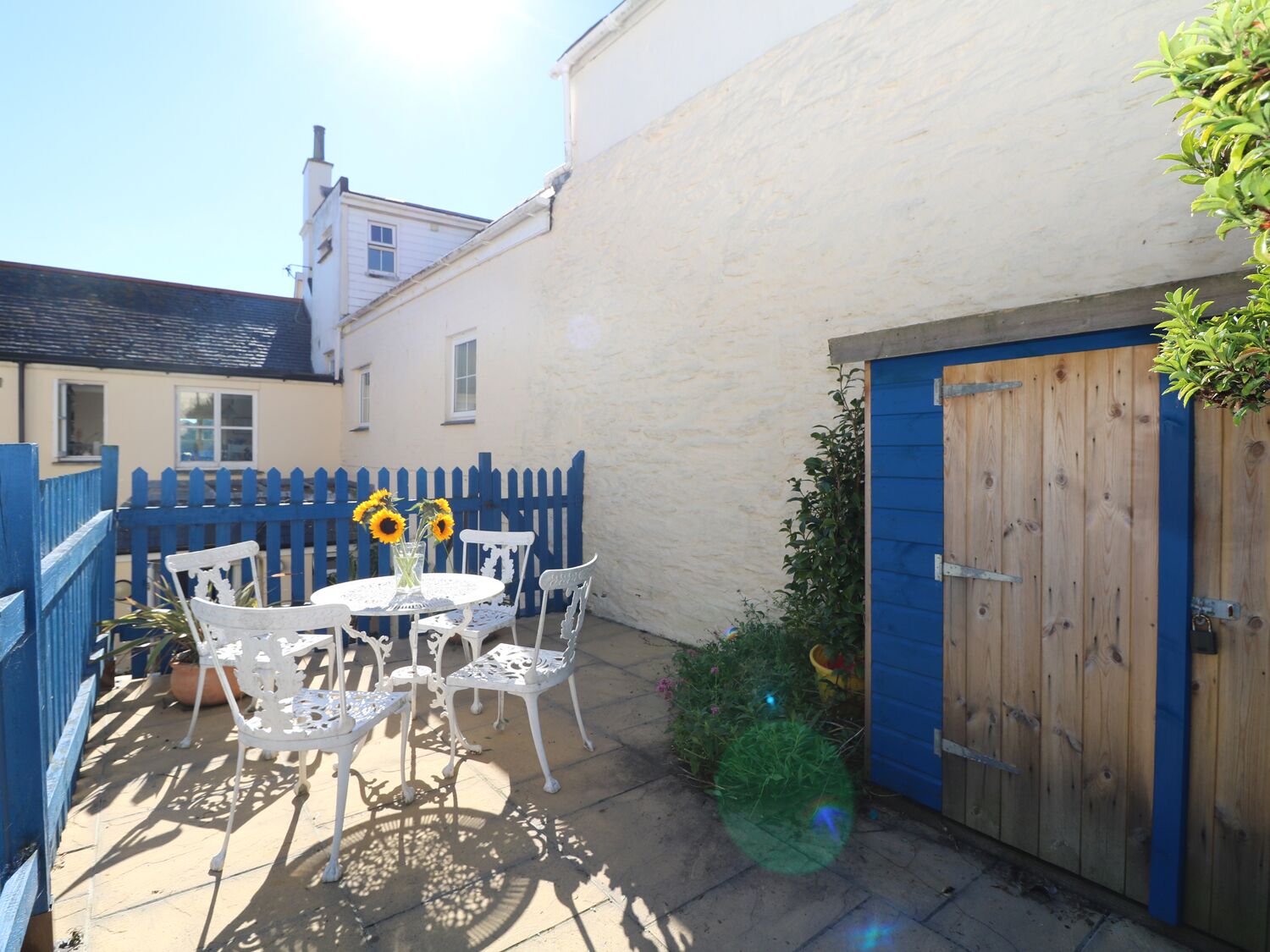 A patio with a round table and white chairs, a blue gate, and a wooden door.