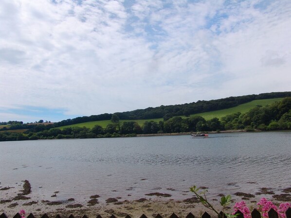 A calm lake with a boat, surrounded by green hills and a cloudy sky.