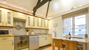 Une cuisine moderne avec un plancher en bois, des armoires blanches, un four encastré et un coin repas avec des chaises en osier.
