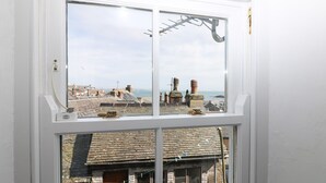 A window with a view of a coastal town, including buildings and a sea view. - Mural Cottage (Penzance)