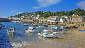 A coastal town with boats docked at the harbor and houses along the hillside. - Mural Cottage (Penzance)