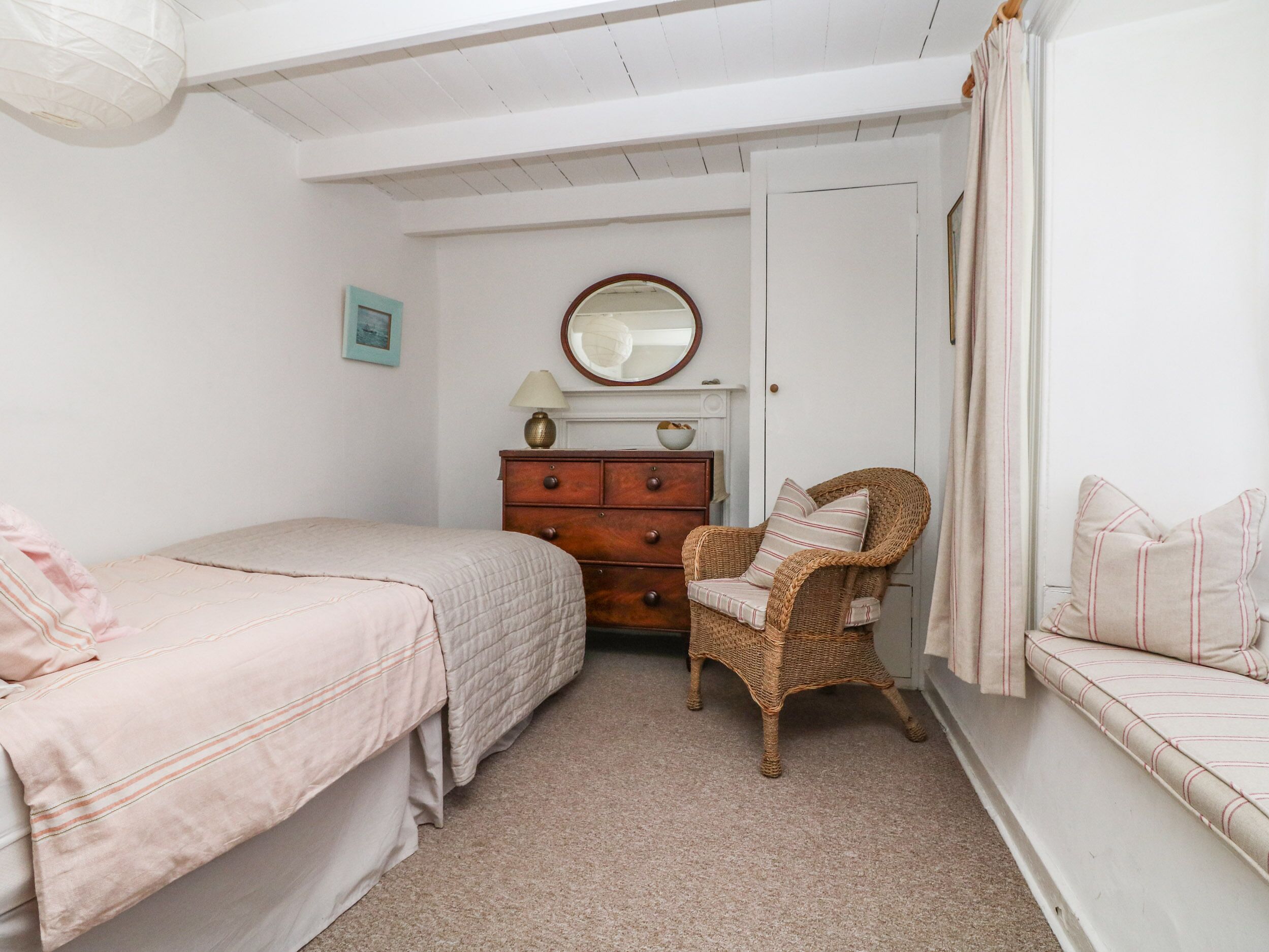 Een slaapkamer met twee bedden, een kaptafel, een rieten stoel en een spiegel aan de muur.