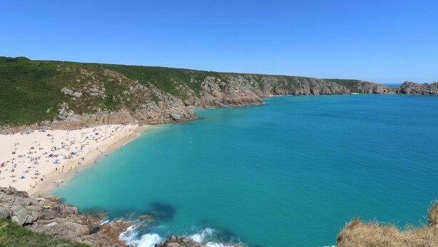 A beach with clear turquoise water, sandy shore, and rocky cliffs. - Mural Cottage (Penzance)