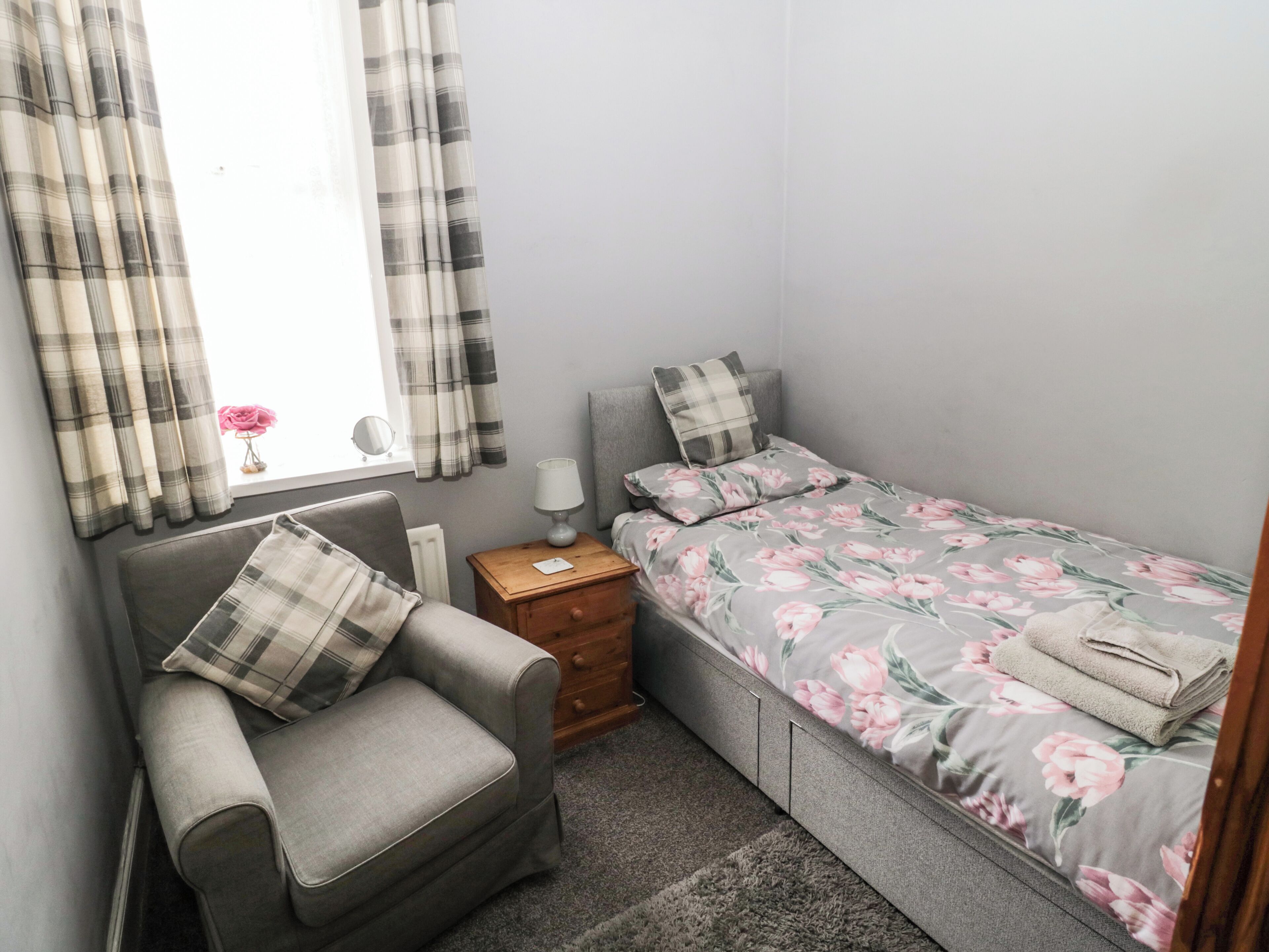 A bedroom with a single bed, a chair, a nightstand, and a window with curtains.
