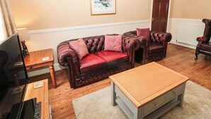 Un salon avec un canapé en cuir rouge foncé, une table basse en bois, un téléviseur et un tableau encadré accroché au mur.