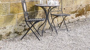 A small outdoor seating area with two metal chairs and a table, set against a stone wall. - Stable Cottage (Whitby)