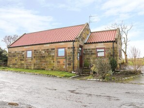 Un bâtiment en pierre avec un toit recouvert de tuiles rouges, un petit porche et une fenêtre donnant sur un beau paysage.