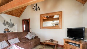 A living room with a brown leather sofa, a television on a wooden stand, and a stone floor. - Stable Cottage (Whitby)