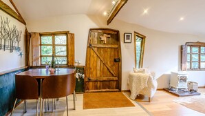 A cozy room with a wooden door, a dining table with chairs, a white cabinet, and a bed with a white blanket. - Brookbank Folly (Mitcheldean)