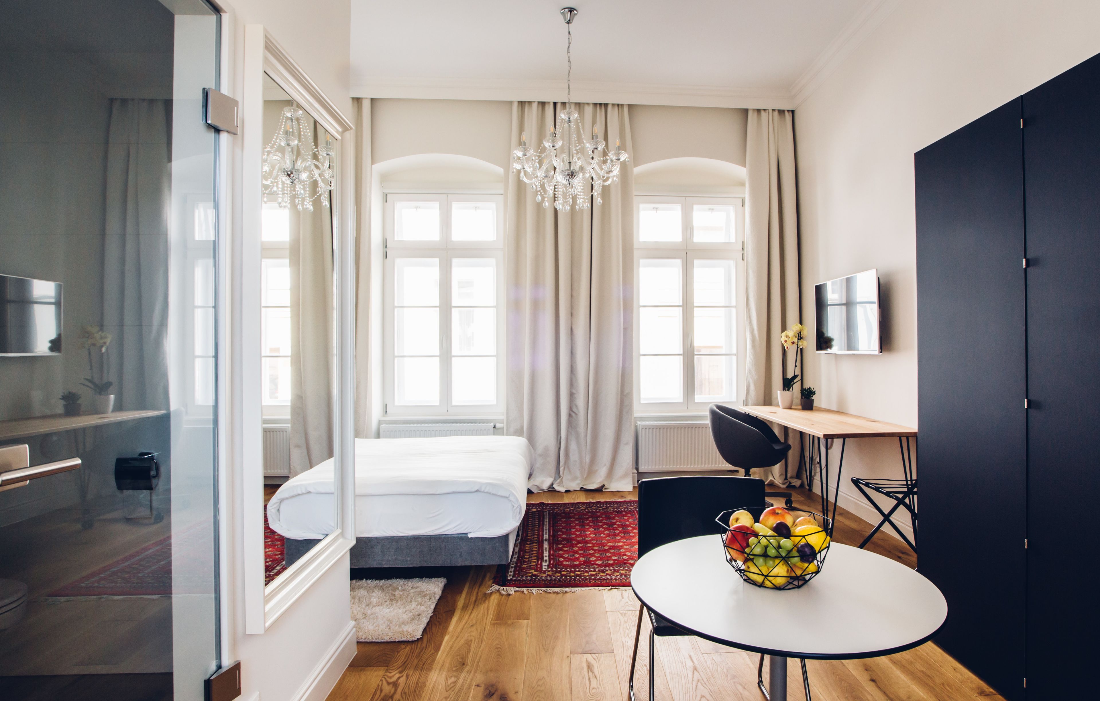 Quarto de hotel moderno com cama, mesa de jantar com frutas, televisão e um guarda-roupa espaçoso.