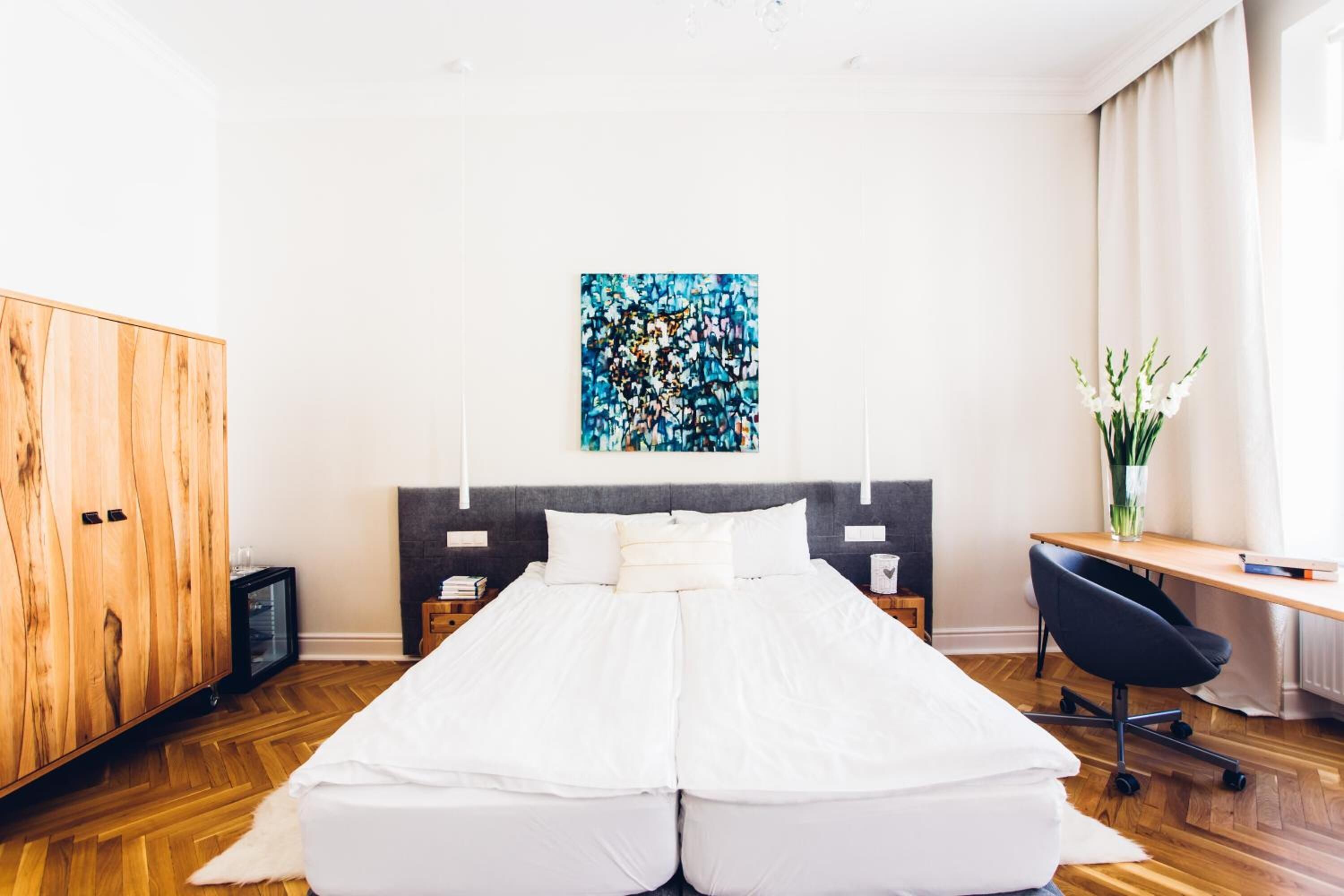 A bedroom with a bed, a desk, a chair, a wardrobe, and a painting on the wall.