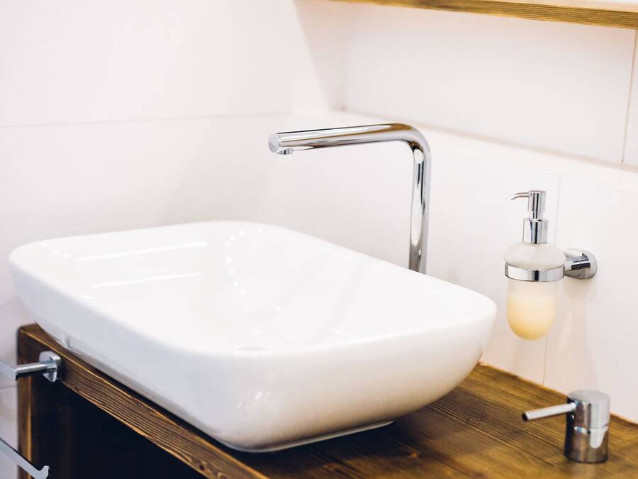 Un baño con lavamanos blanco, grifo cromado y tocador de madera.