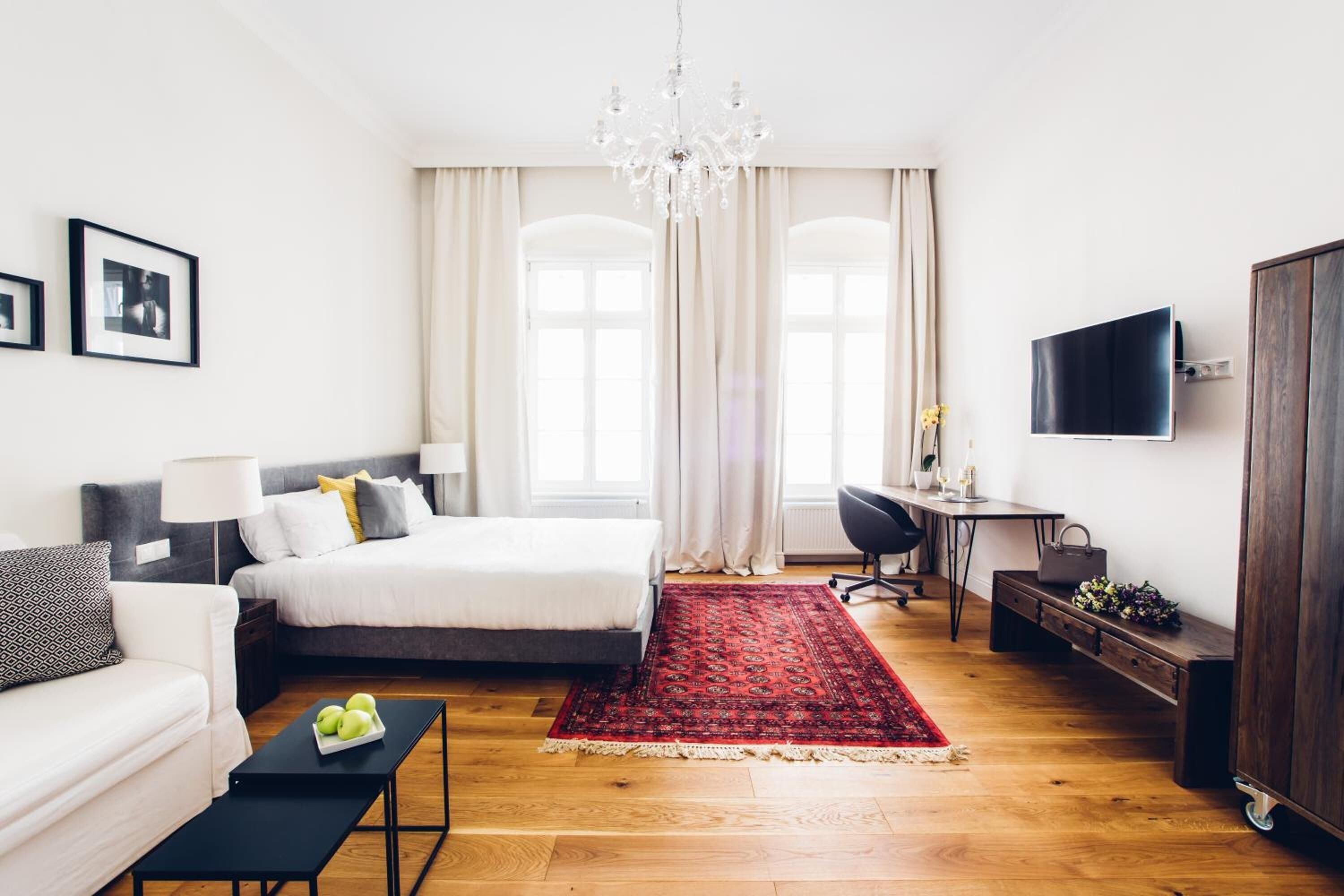 Quarto moderno com cama, mesas de cabeceira, escrivaninha, televisão e lustre.