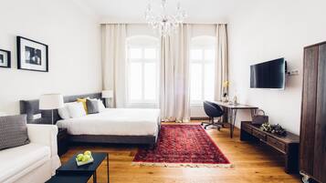 Quarto moderno com cama, mesas de cabeceira, escrivaninha, televisão e lustre.
