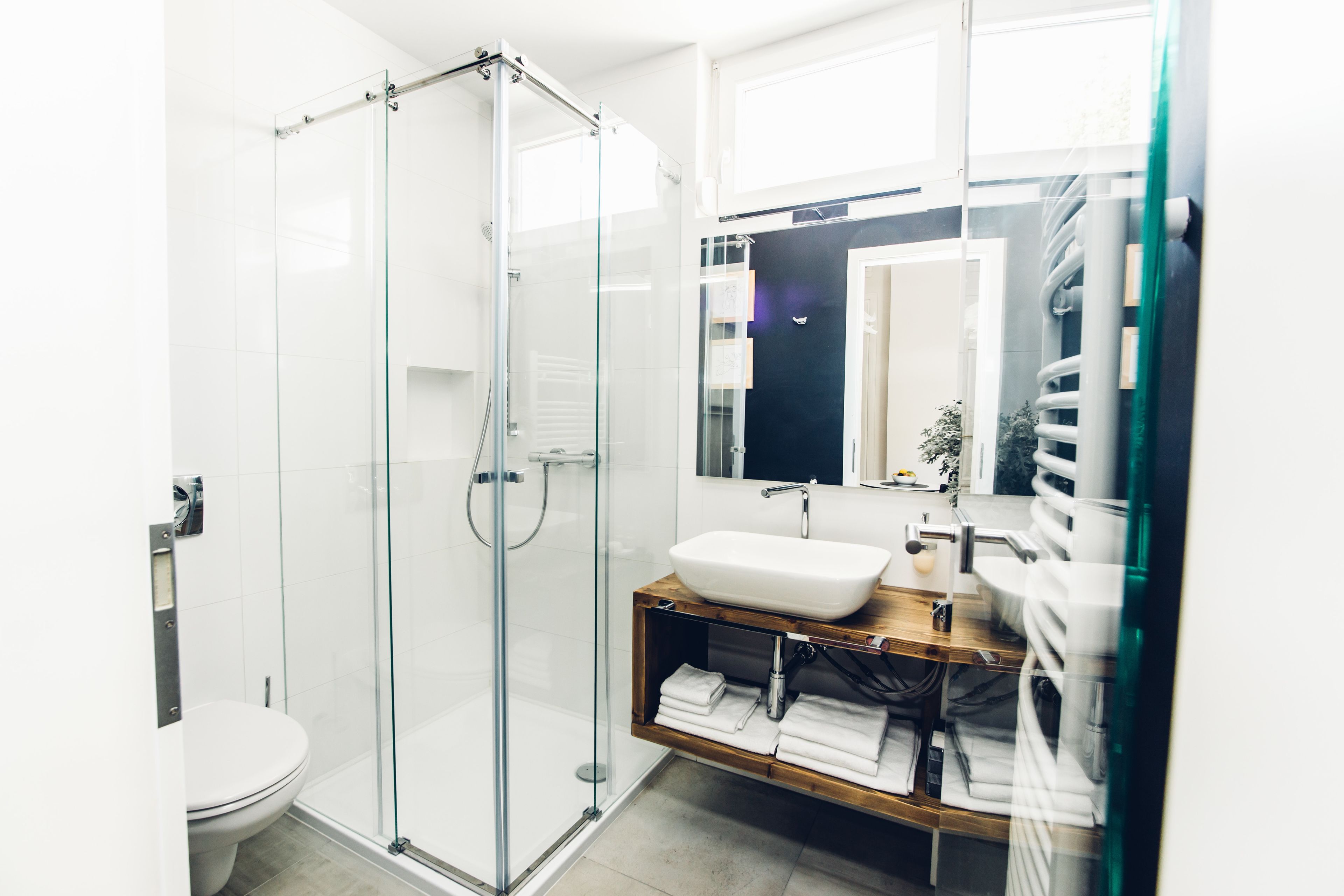 Un bagno moderno con cabina doccia in vetro, lavandino bianco e mobile vanitario in legno.