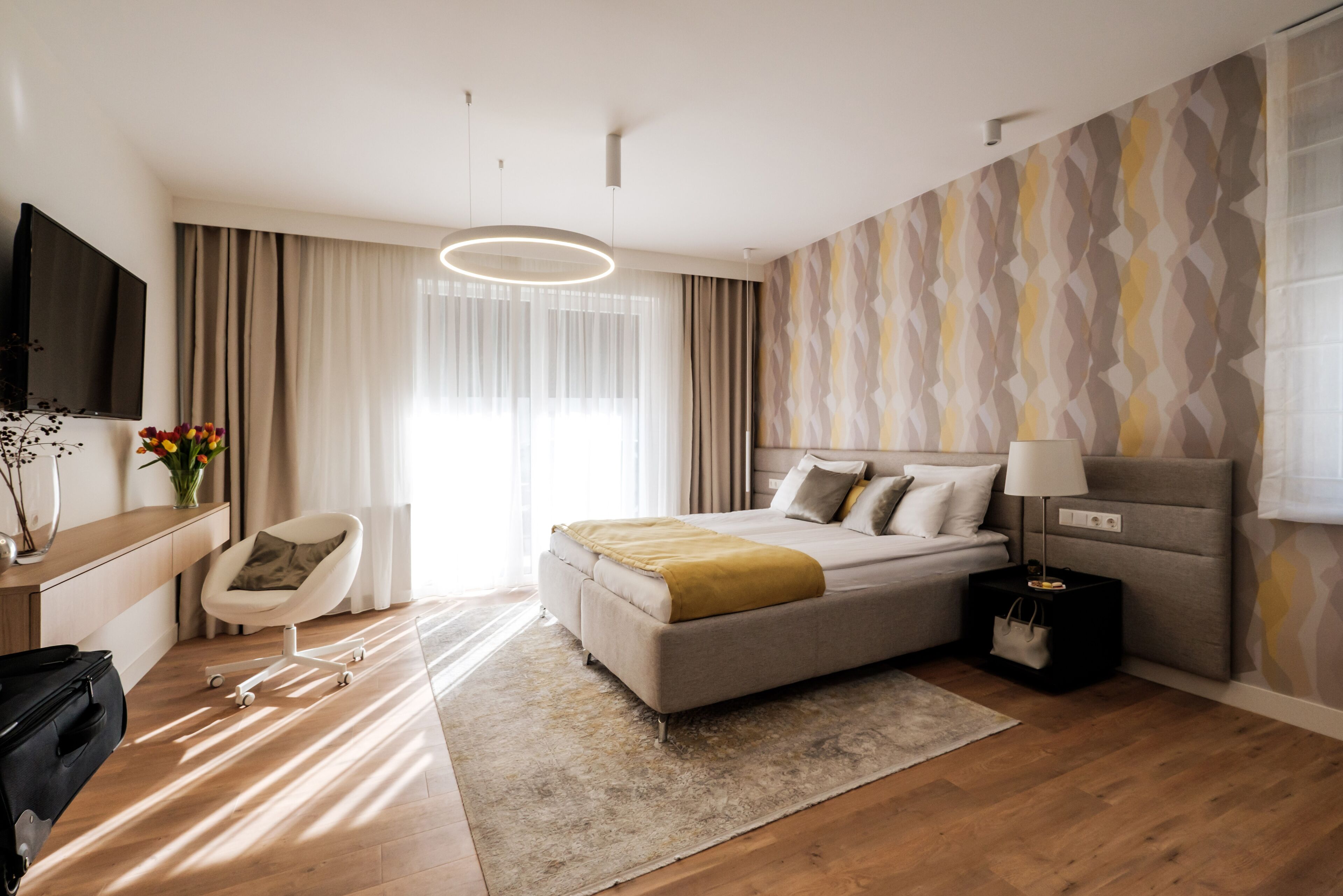 Una habitación de hotel moderna con cama, mesita de noche, lámpara y televisor.