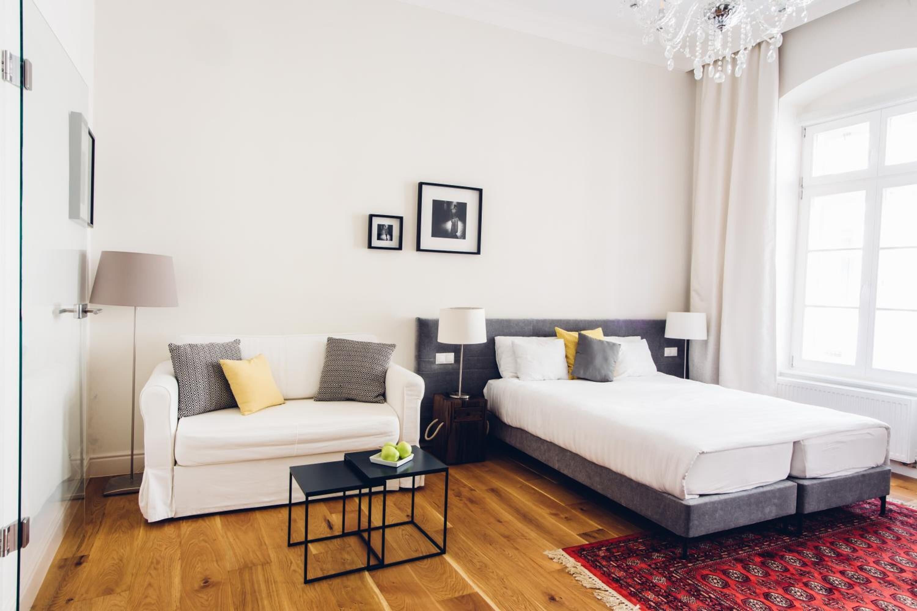 Et moderne hotelværelse med en hvid sofa, en seng, et lille bord med æbler og to billeder hængende på væggen.