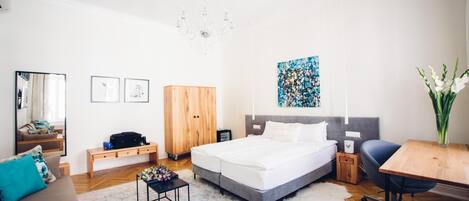 A modern bedroom with a large bed, a desk, a chair, a wardrobe, and a chandelier.