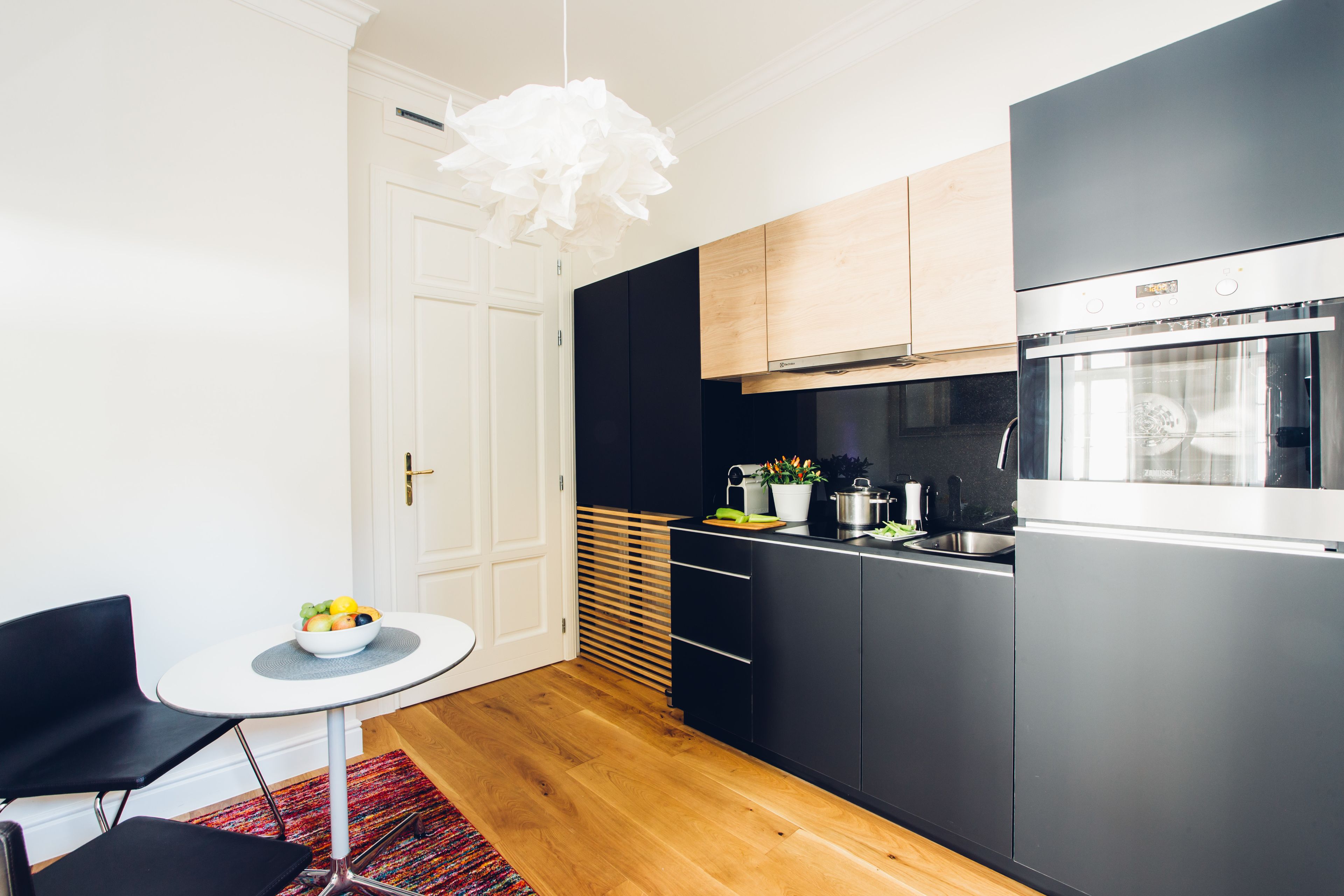 A modern kitchen with black cabinets, a stainless steel oven, and a white pendant light.