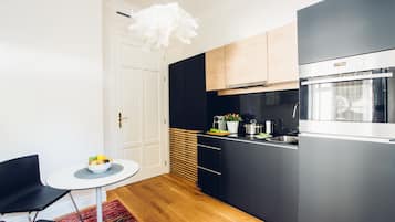 A modern kitchen with black cabinets, a stainless steel oven, and a white pendant light.