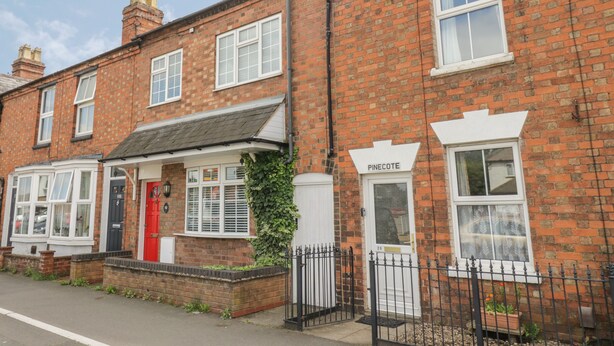 A row of terraced houses with a red door, white windows, and a sign reading "PINECOTE".