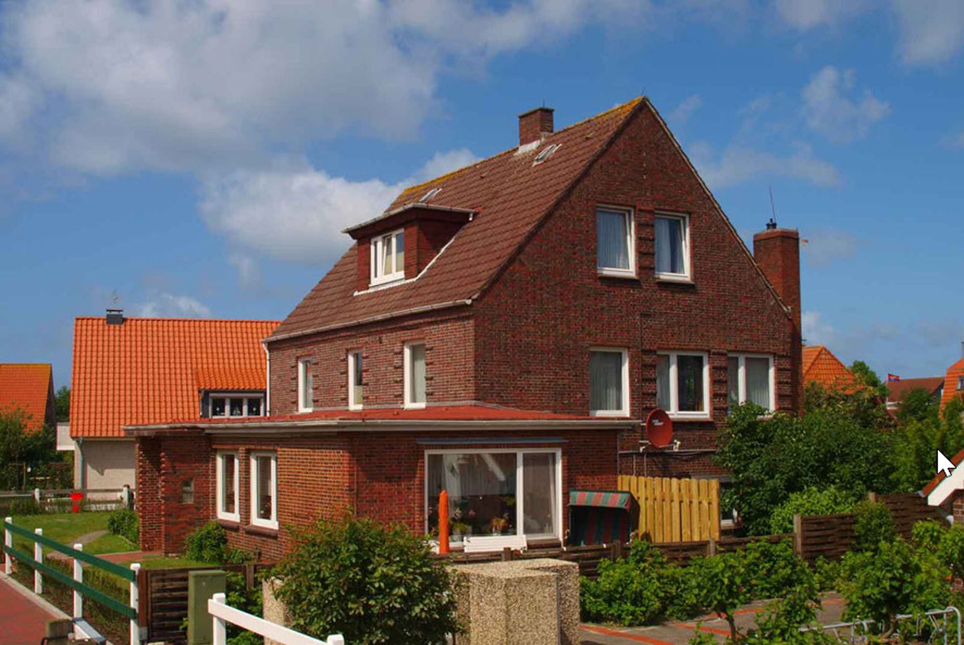 A two-story brick house with a sloped roof, multiple windows, and a visible chimney.