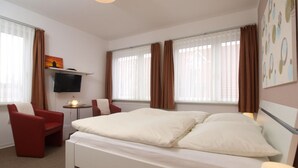 Una habitación de hotel con una cama, televisión, una silla y una mesita.