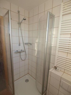 A bathroom with a shower, tiled walls, a toilet, and a radiator. - Pension Friedrich Voss (Langeoog)