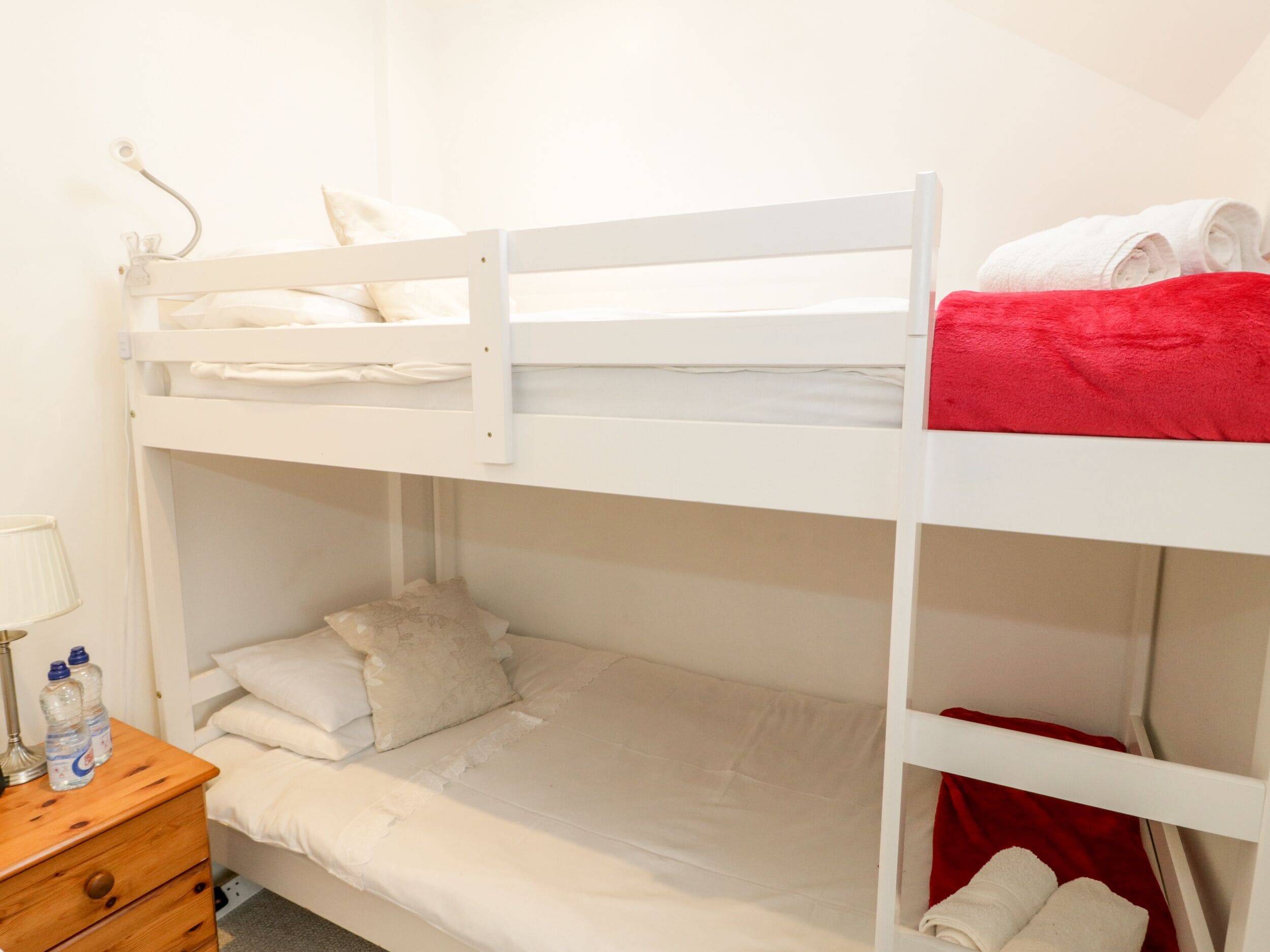 Quarto com beliche, mesa de cabeceira de madeira, abajur e cobertor vermelho.