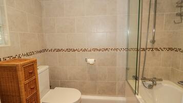Une salle de bain comprenant des toilettes, un meuble en osier, une douche fermée par des parois de verre et une baignoire.