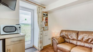 Een kitchenette met een magnetron, een houten kast en uitzicht door een glazen deur op een balkon.