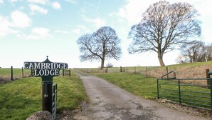Un camino rural que lleva a Cambridge Lodge, con un muro de piedra y una reja metálica.