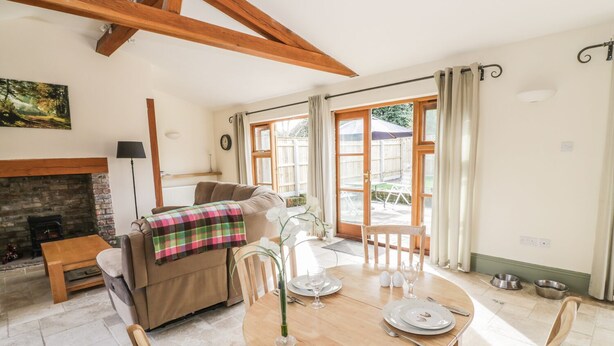 Una sala de estar acogedora con chimenea, un sofá, una mesa de comedor con sillas y un ventanal con cortinas.