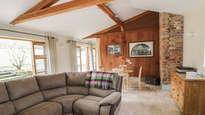 Una sala de estar acogedora con un sofá modular, vigas de madera, una chimenea de ladrillo y una zona de comedor con mesa y sillas.