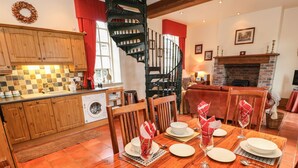 A dining area with a wooden table set for four, a kitchen with wooden cabinets, a washing machine, and a spiral staircase. - The Old Chapel (Chesterfield)