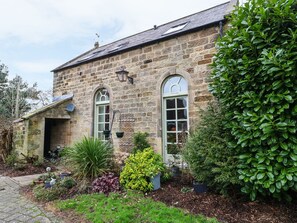 A stone building with two arched windows, a small door, and a garden with various plants. - The Old Chapel (Chesterfield)